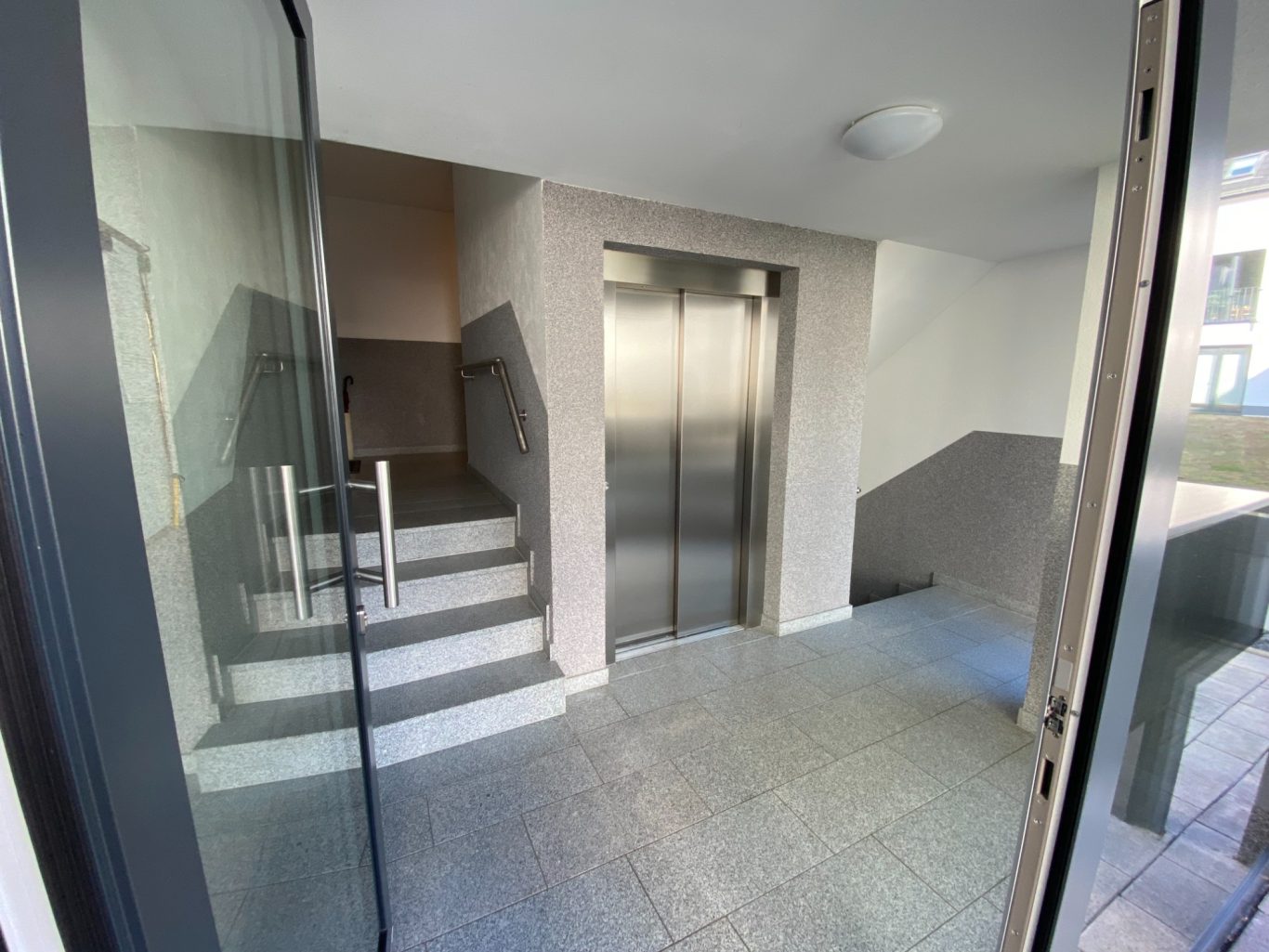 Eingangsbereich mit Treppen und einem Aufzug im Hintergrund.