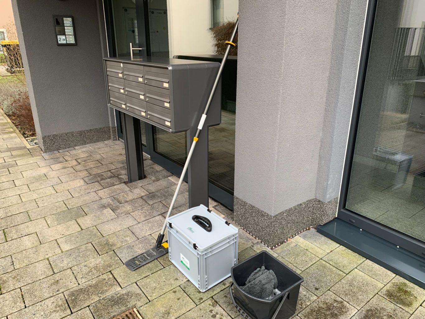 Gut geordnete und saubere Reinigungsutensilien auf dem Pflasterstein- Fußweg vor einem modernen Wohngebäude