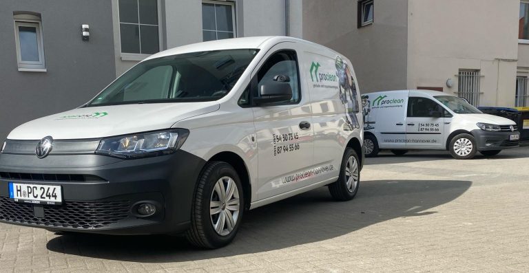 Zwei Lieferwagen, einer weiß mit Logo, geparkt auf einem gepflasterten Bereich.