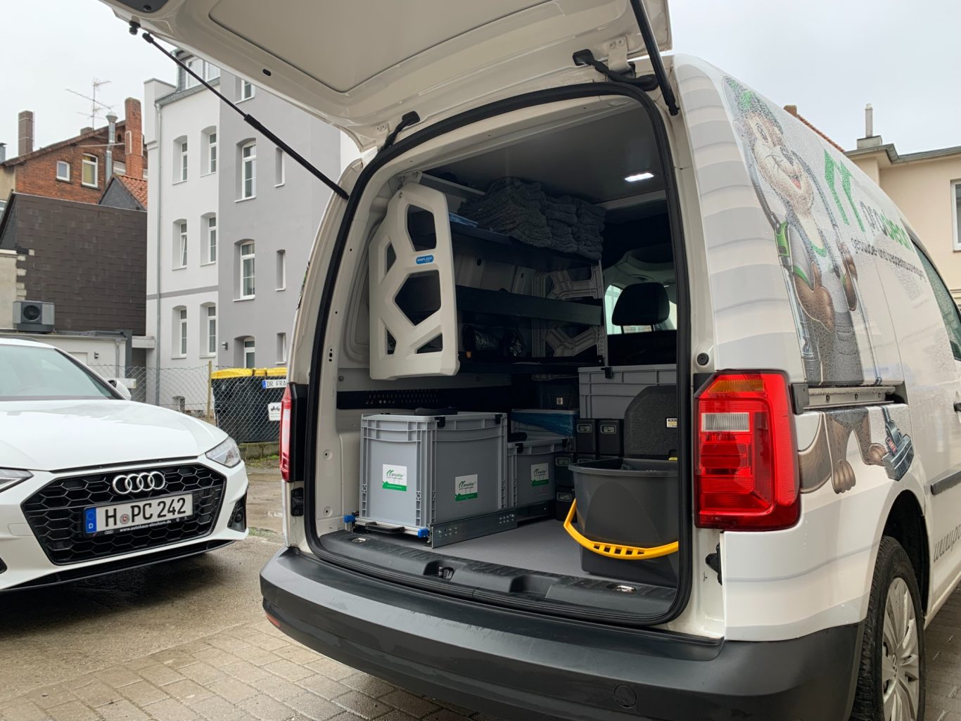 Transporter mit einer offenen Heckklappe, ausgestattet mit Kisten und Regalen.