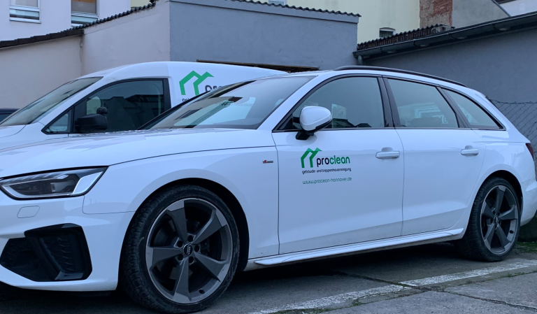 Weißer Audi Sportwagen neben einem weißen Lieferwagen Caddy SA vor einem Gebäude, beide Wagen mit dem Logo von Proclean versehen.